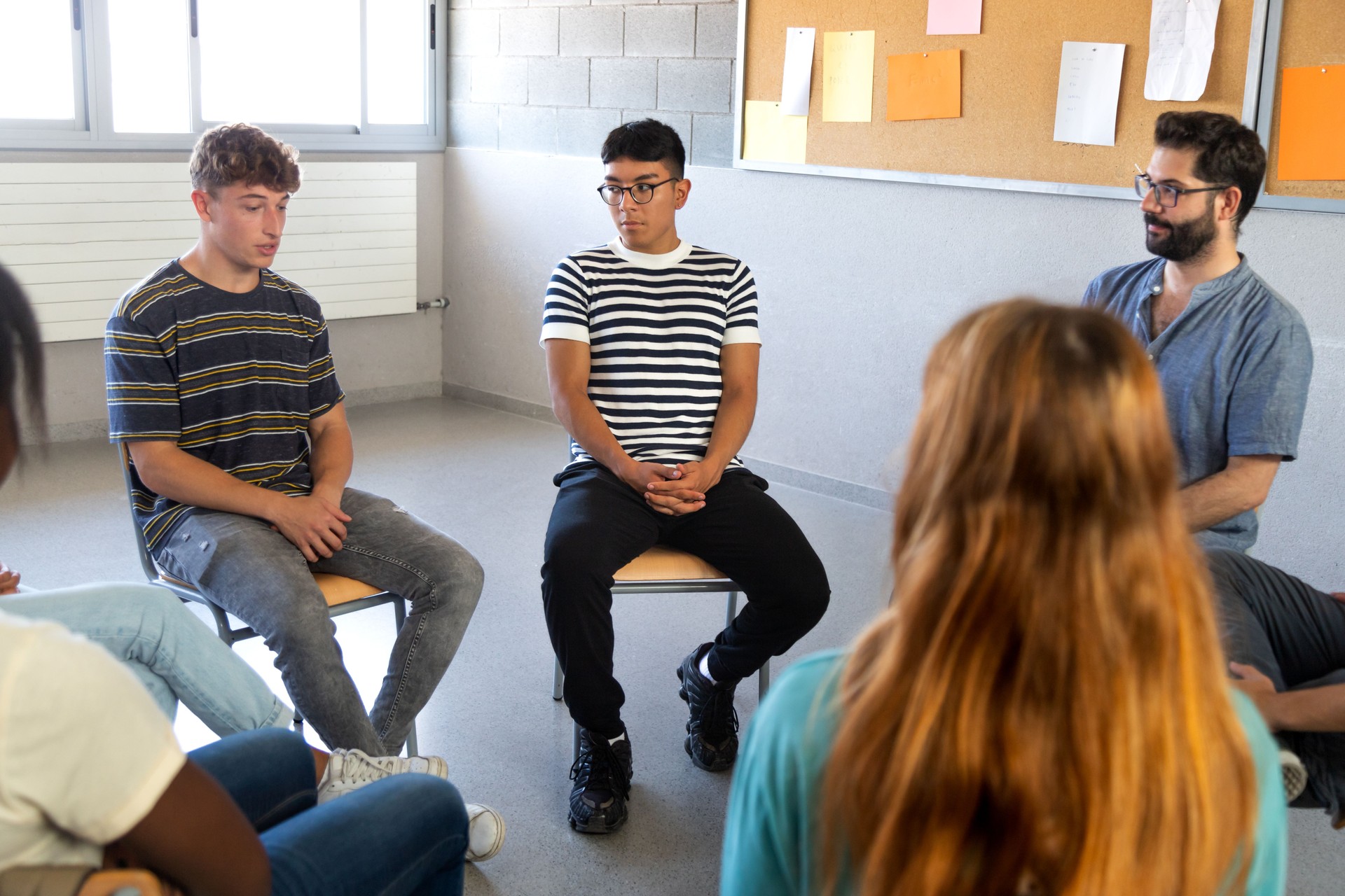 Multiracial students sitting in a circle sharing problems with classmates and teacher. High school support group.